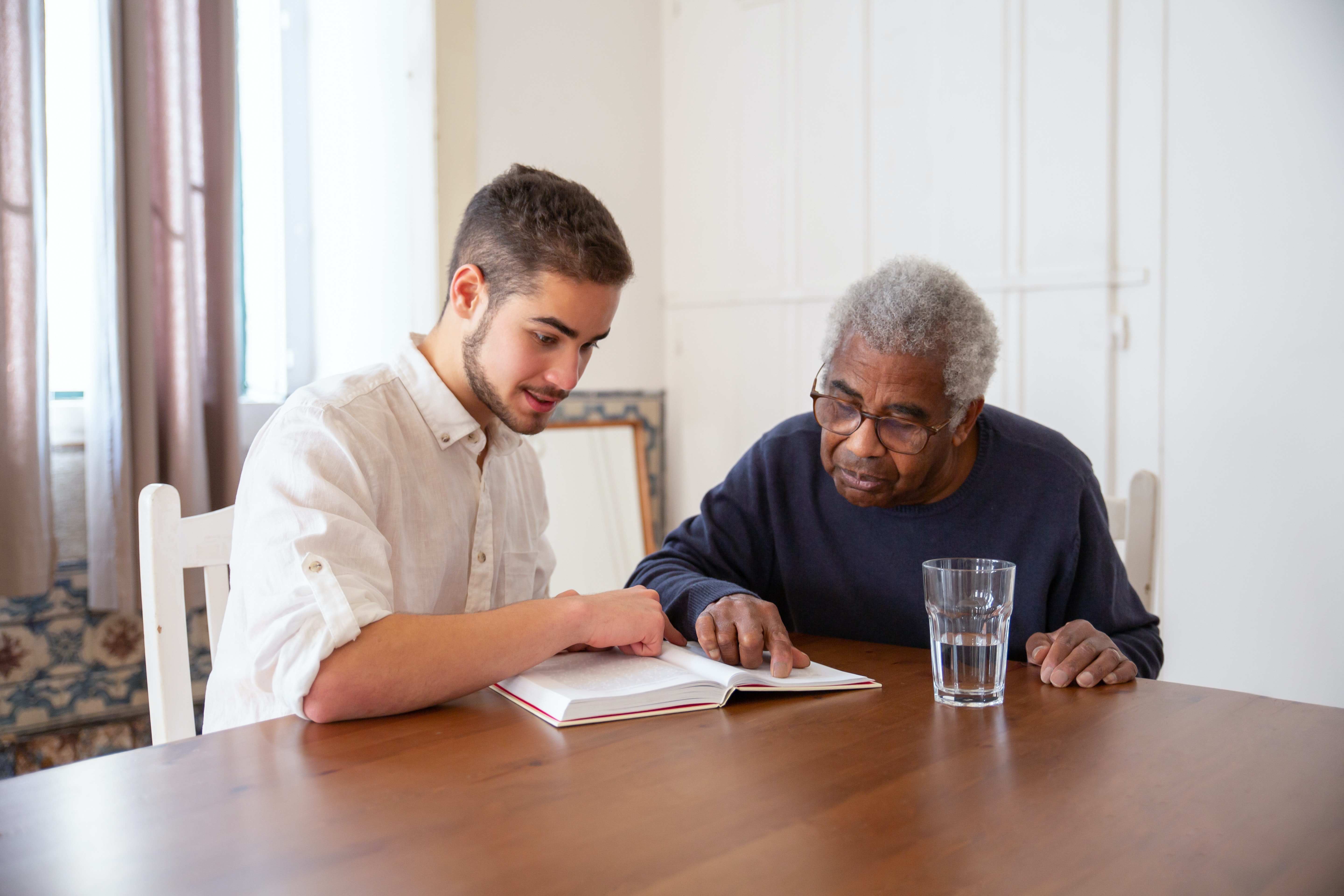 Joven leyendo un libro junto a un hombre mayor en una mesa