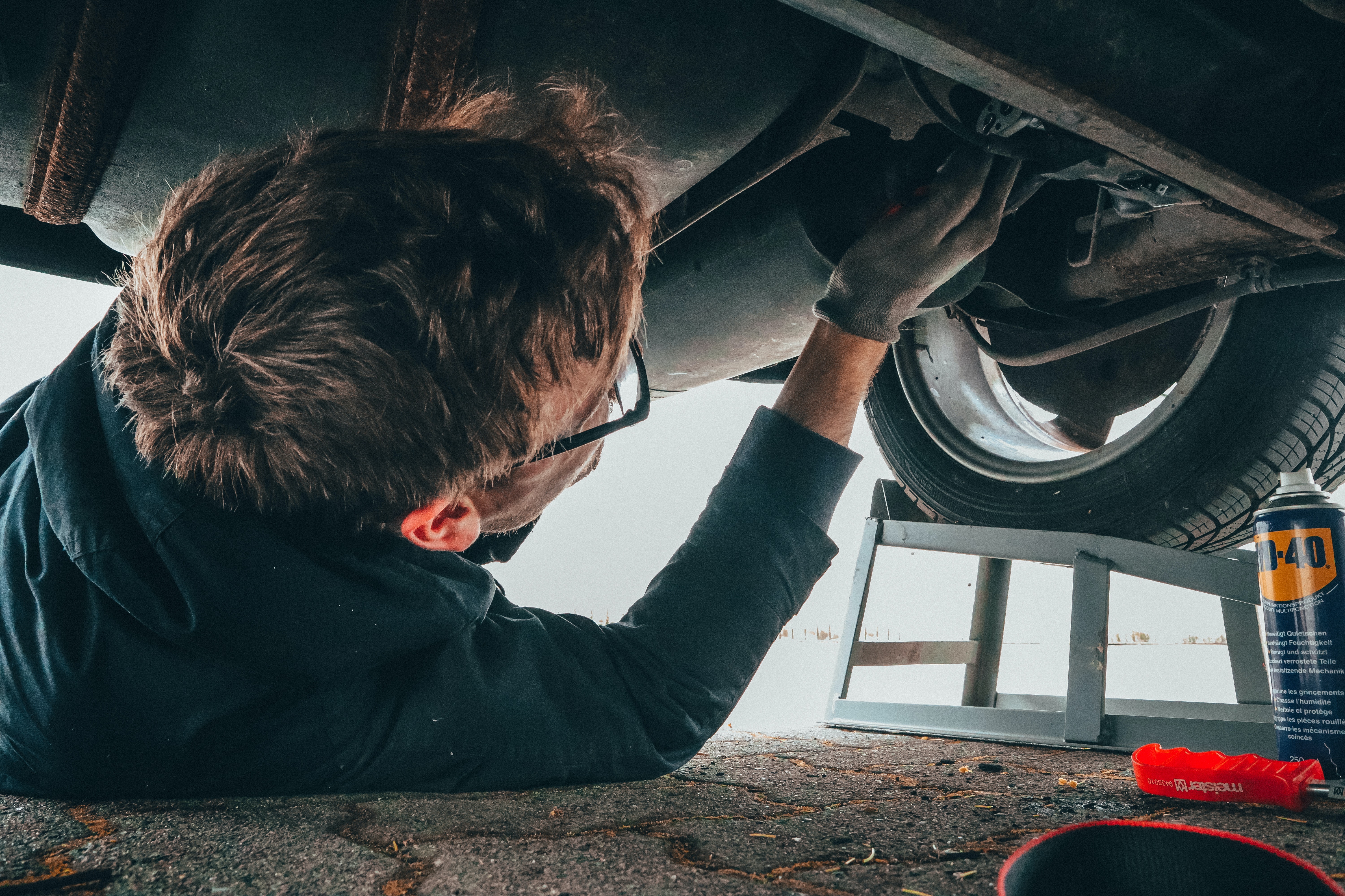 Mecánico acostado bajo un automóvil realizando reparaciones con herramientas cerca