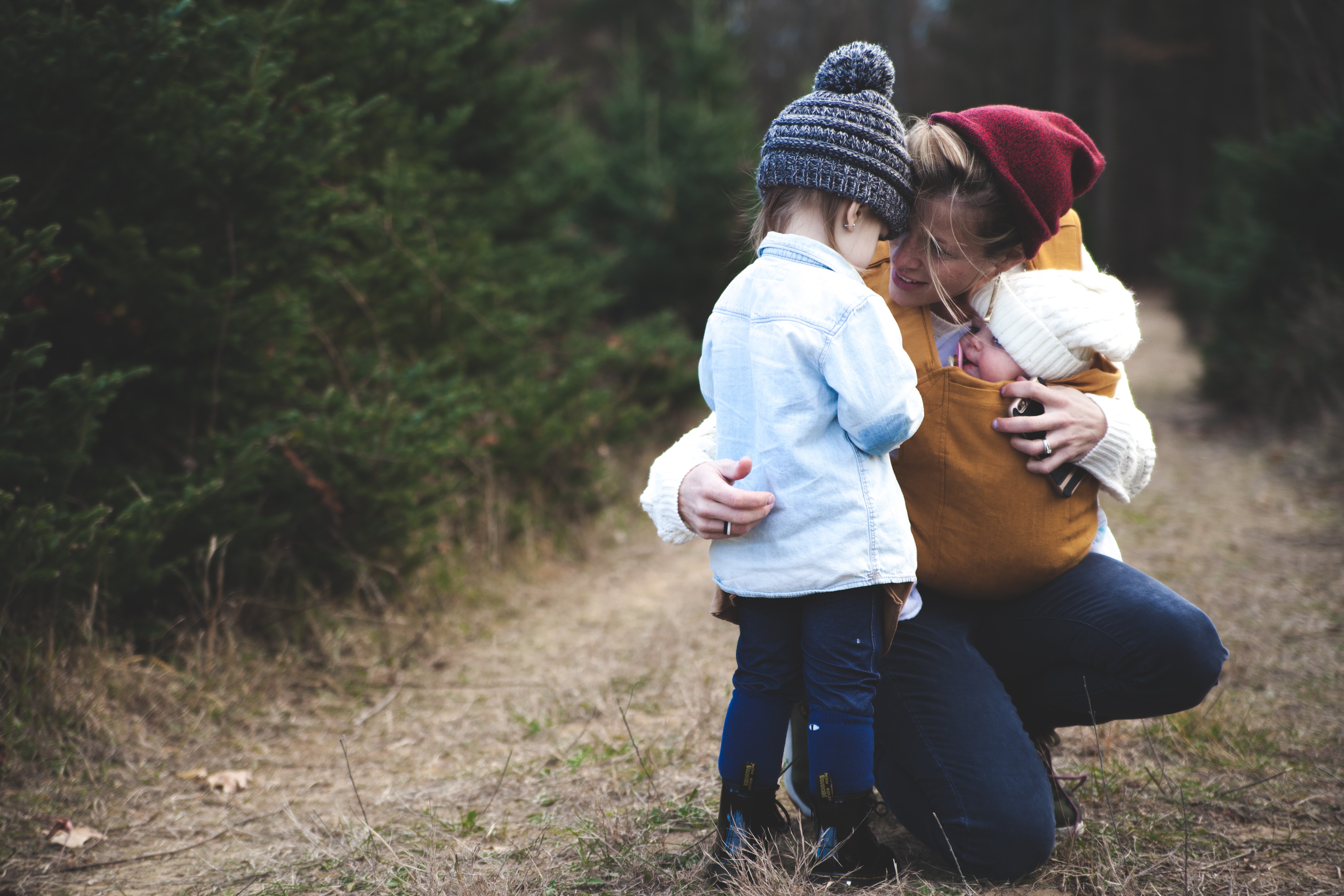 Madre agachada abrazando a sus hijos pequeños en un camino del bosque