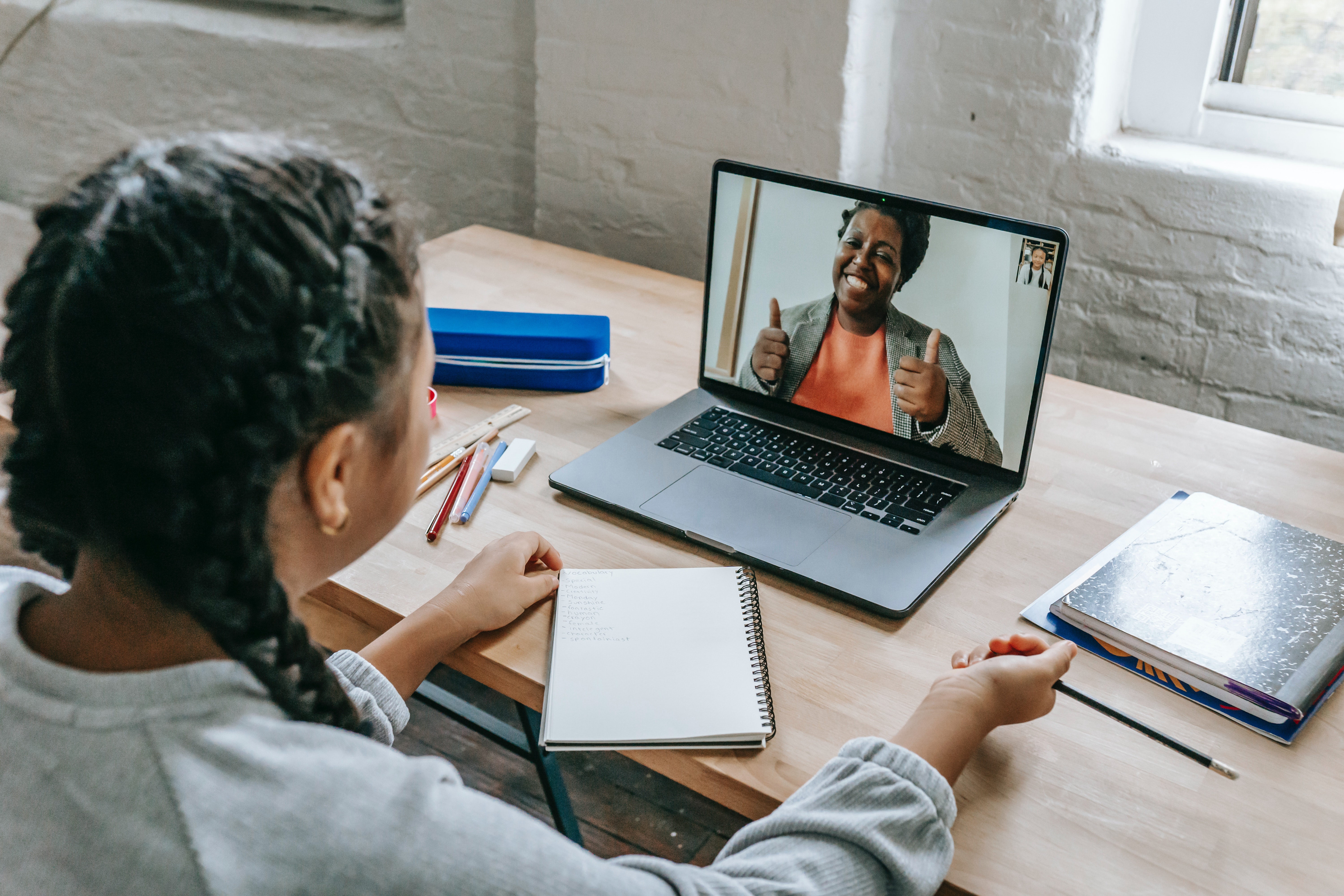 Estudiante tomando una clase virtual mientras conversa con su profesora por videollamada