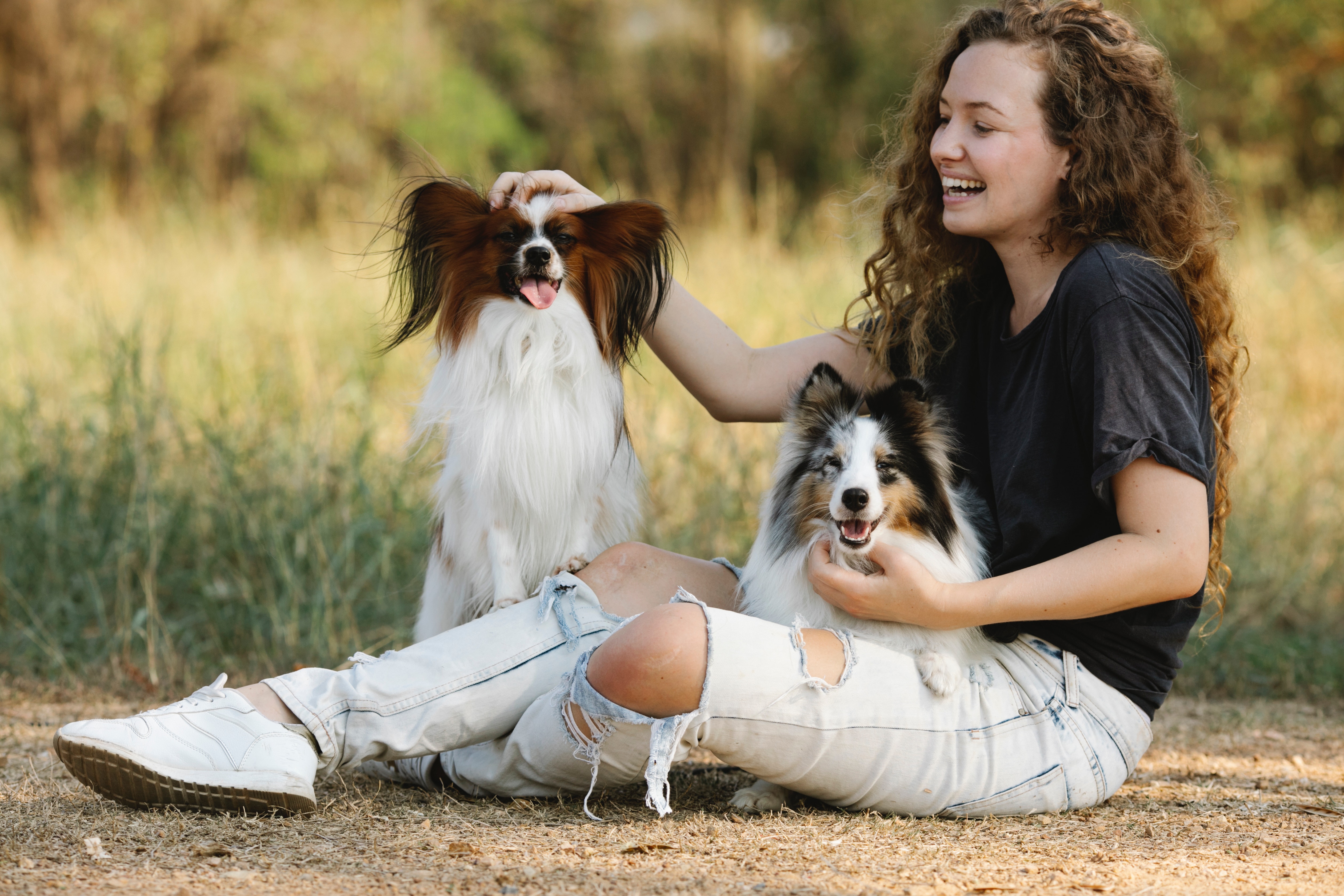Mujer sentada en el campo acariciando a dos perros felices mientras sonríe