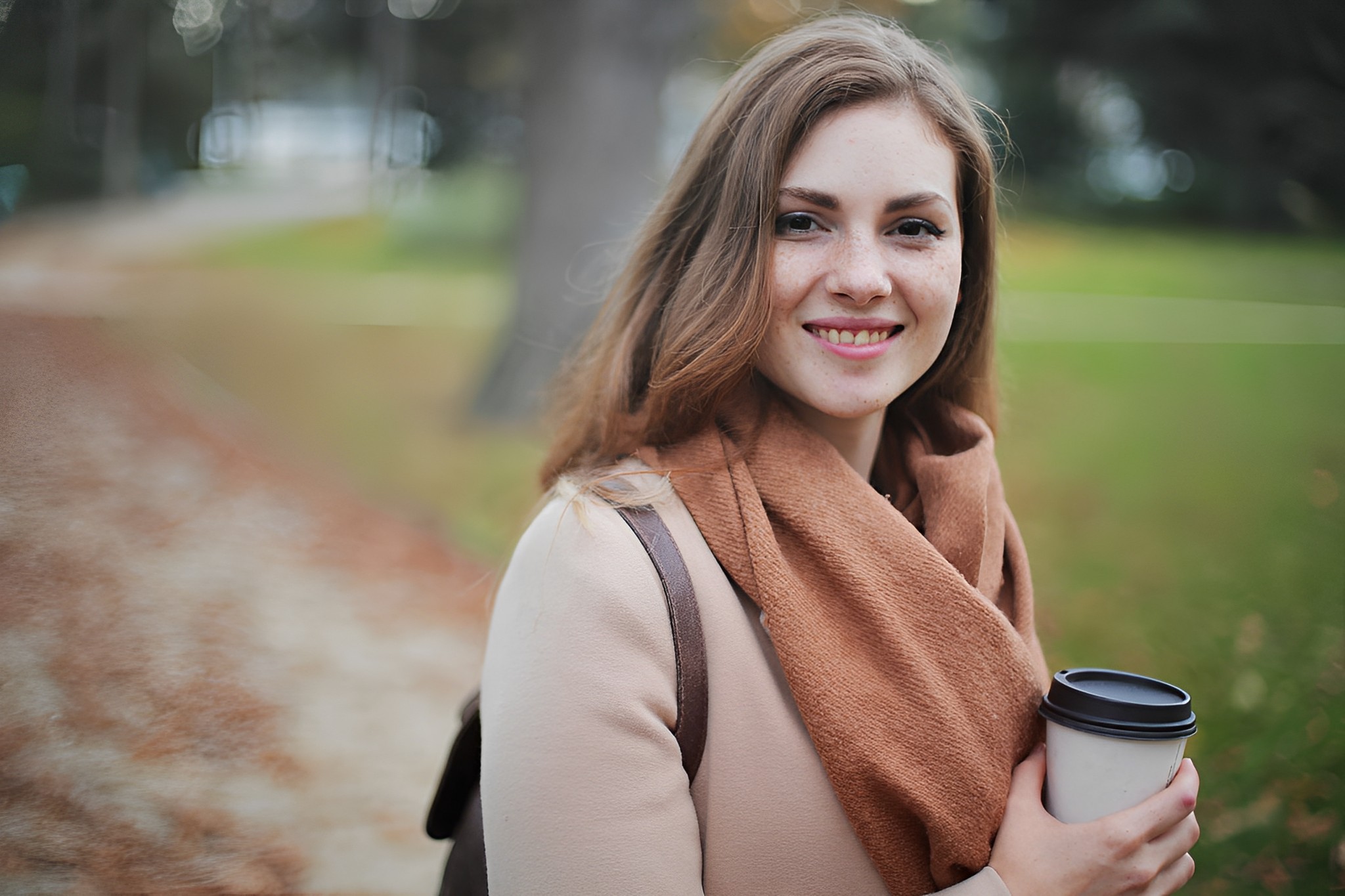 Mujer joven sonriendo con una taza de café en la mano en un parque de otoño